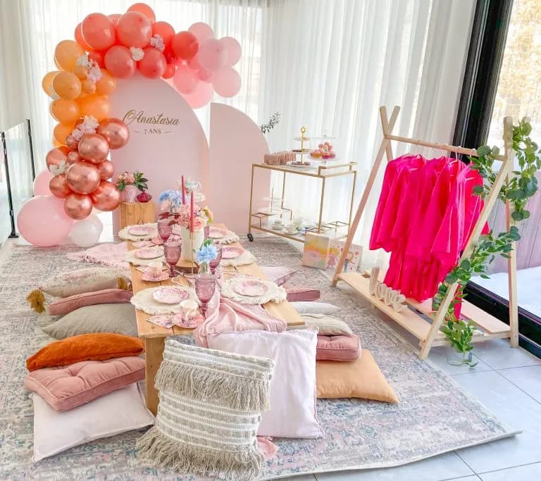 Fête pyjama d'anniversaire enfant avec arche pêche et corail, coussins et portant de peignoirs roses